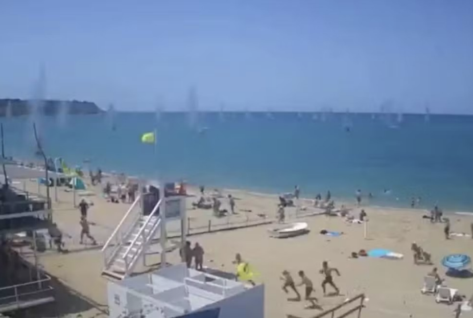 praia com várias pessoas correndo do mar por estar sendo atacado