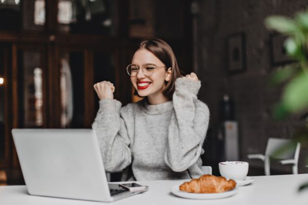 Mulher sentada em uma mesa olhando para o computador feliz e comemorando